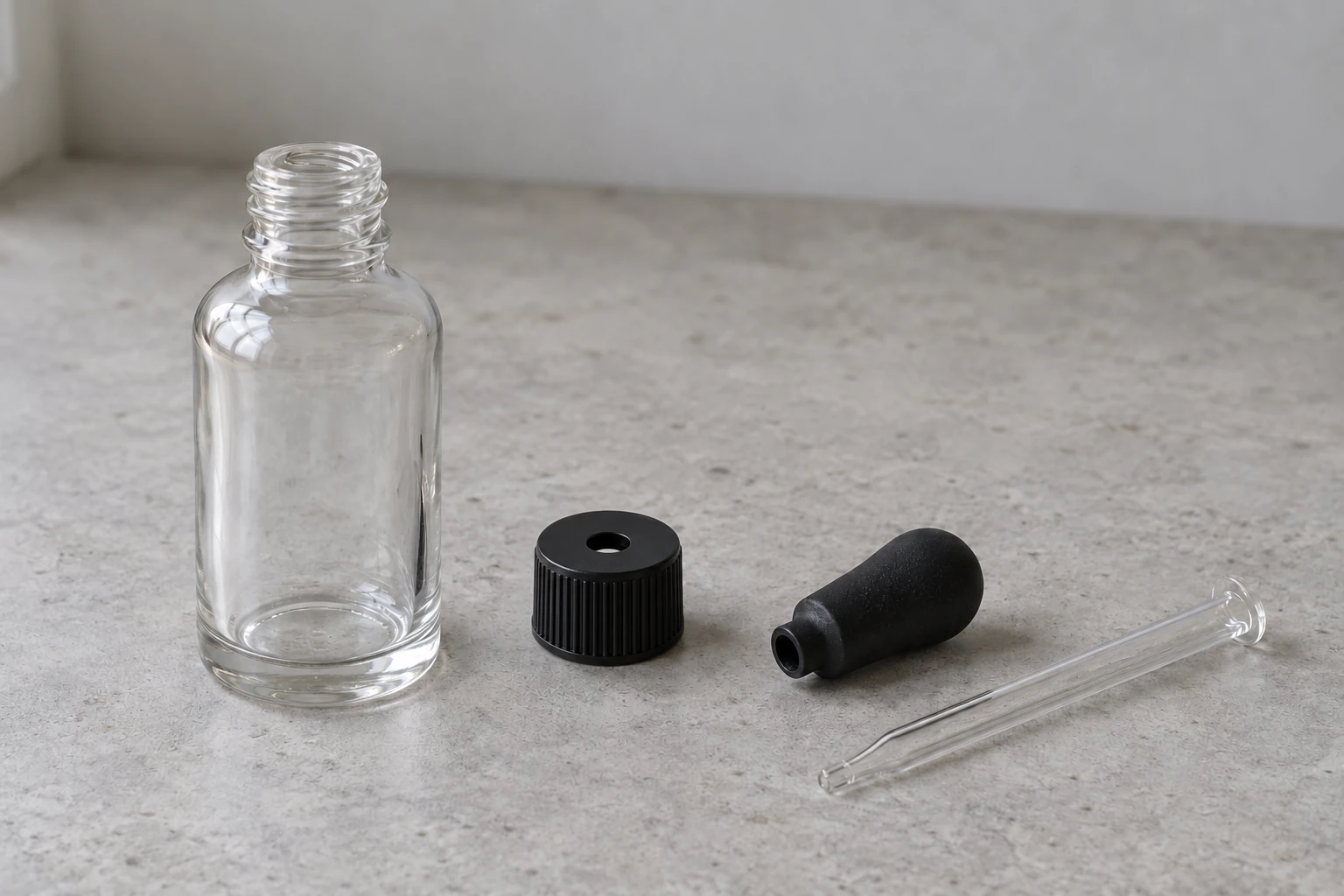 Illustration of an empty glass bottle, black screw collar, separate rubber bulb and clear glass pipette laid flat on a bench
