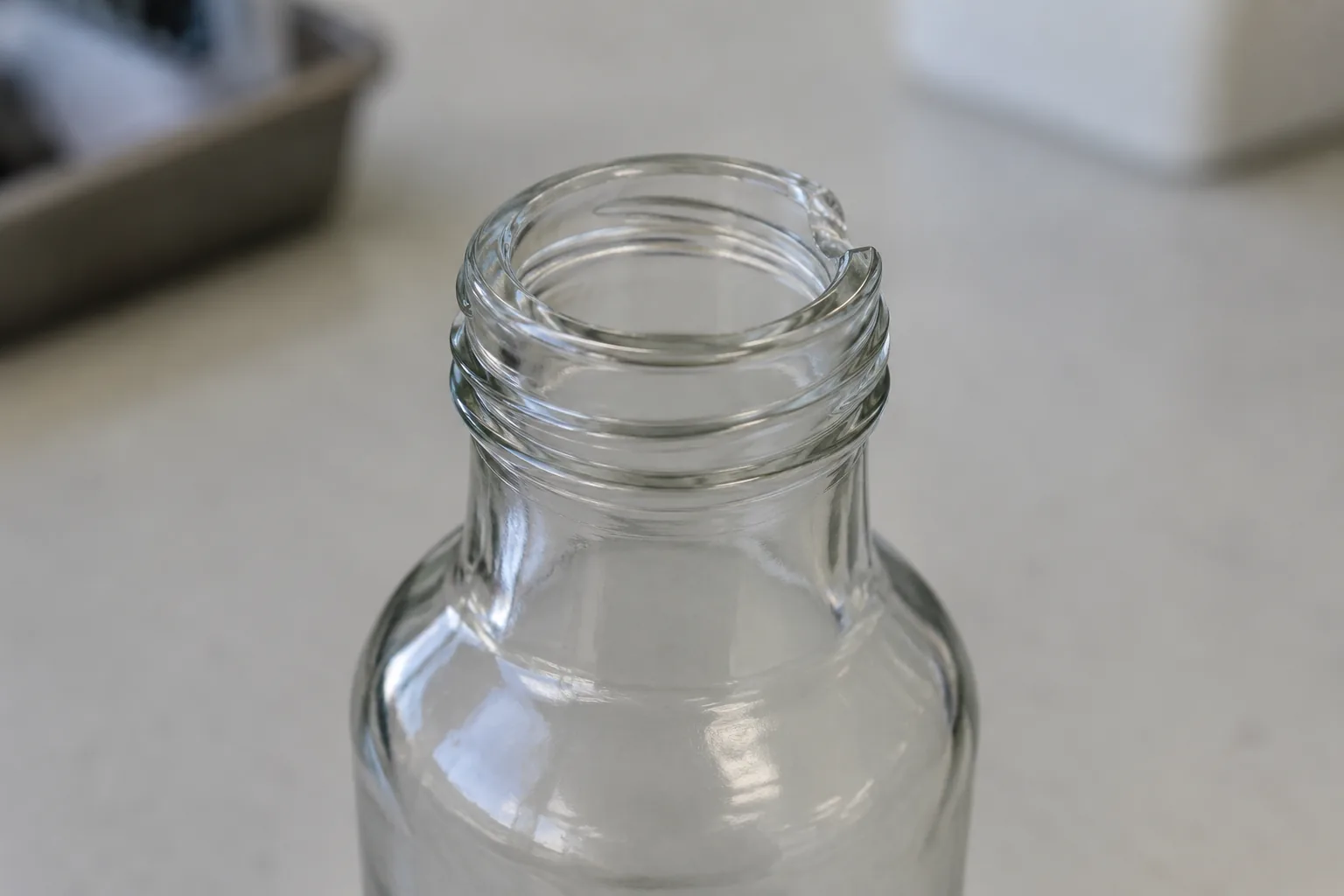 Close view of a clear threaded bottle mouth with a small missing area at the rim
